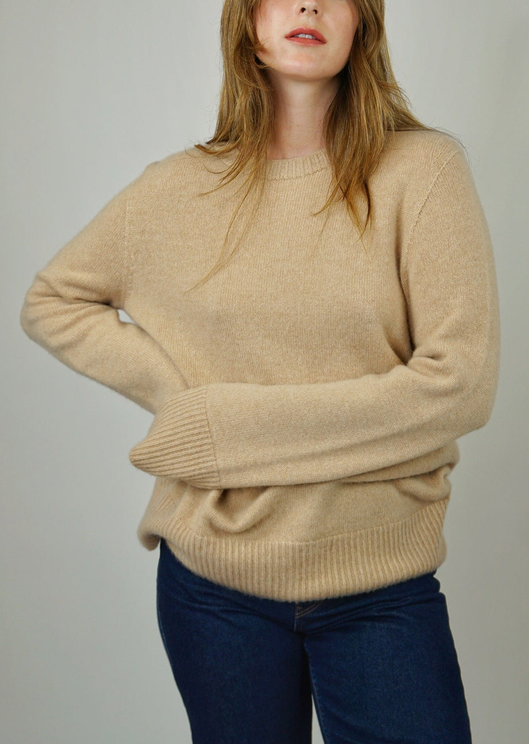 A woman wearing a beige cashmere sweater with rib trim details, paired with blue jeans.